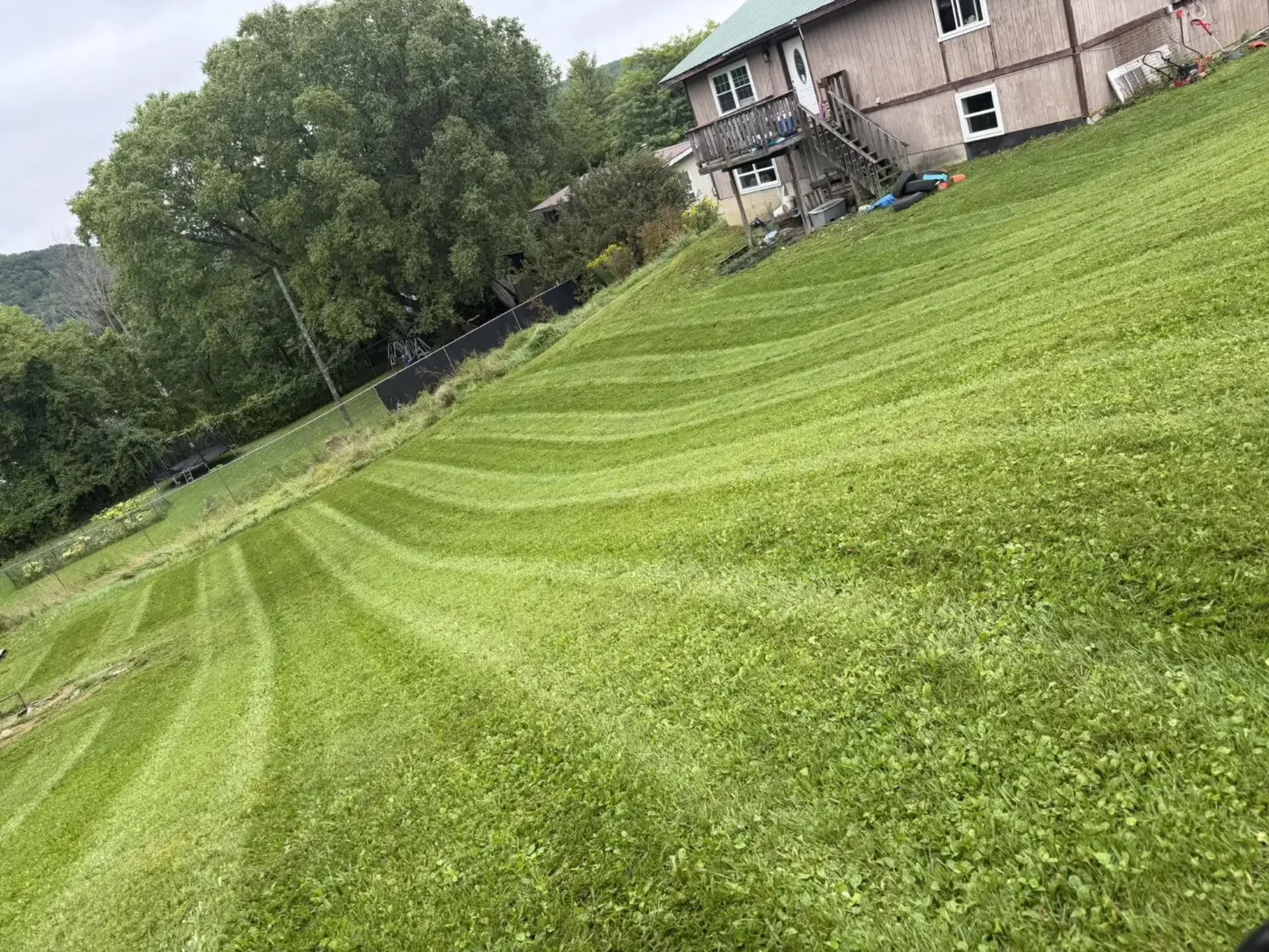 A large hillside lawn freshly mowed with clean stripes by EK Services